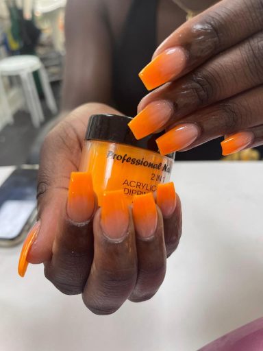Een hand met lange, oranje nagels houdt een potje oranje nagellak vast.