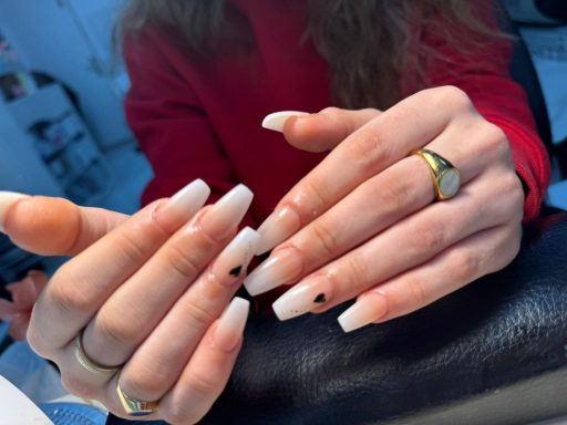 Vrouwelijke handen met lange, witte nagels en zwart hartje op een nagel.