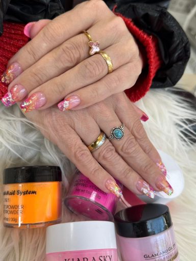 Vriendelijke handen met kleurrijke nagels, verschillende potjes nagelproducten eromheen.