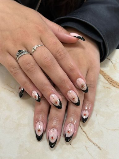 Nagels met een roze basis en zwarte tips, versierd met een bloemmotief.